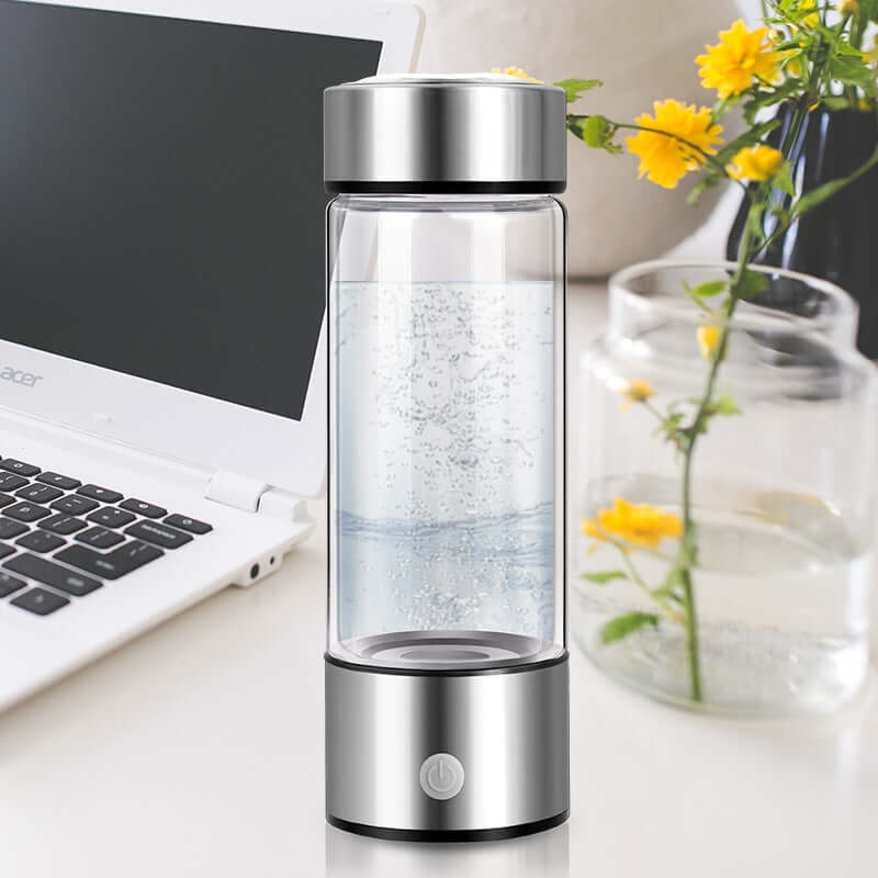 Stainless steel electric water bottle next to a laptop and glass vase with yellow flowers