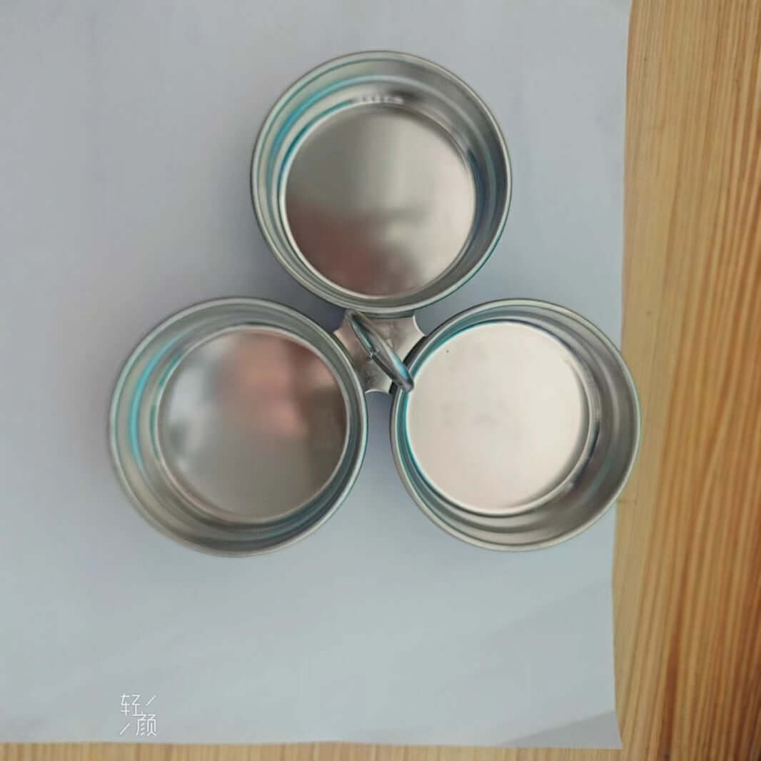 Three round stainless steel spice containers with lids, arranged on a wooden surface