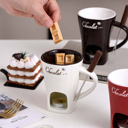 Hand placing chocolate pieces into a ceramic fondue mug with candle, dessert in background