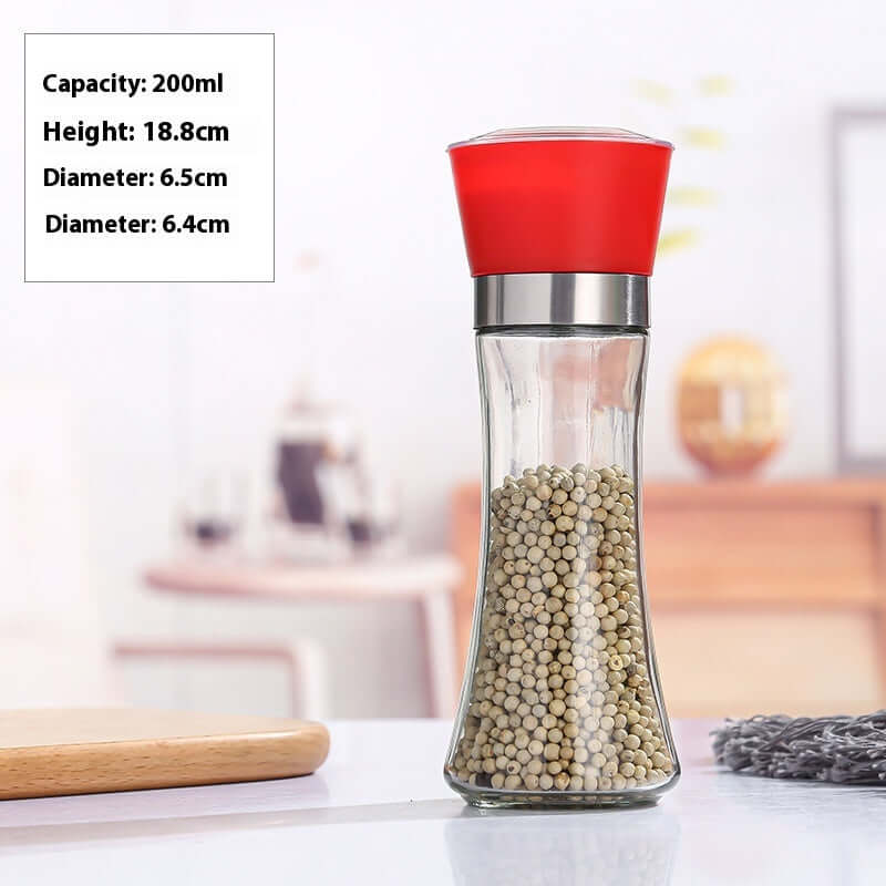 Glass pepper grinder with red lid, filled with whole peppercorns, on kitchen countertop