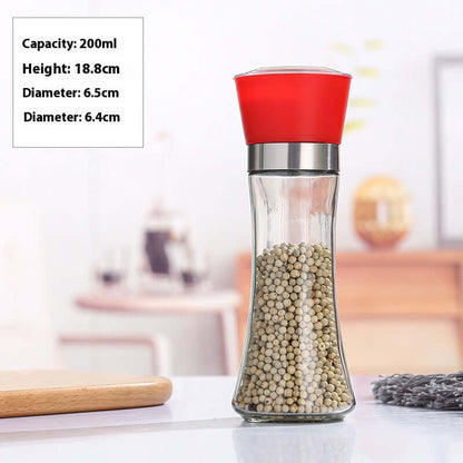 Glass pepper grinder with red lid, filled with whole peppercorns, on kitchen countertop