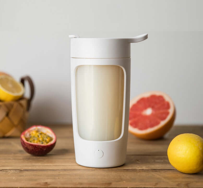 White portable blender cup on wooden table with grapefruit, lemon, and passion fruit