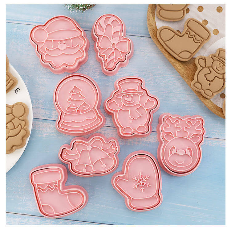 Set of pink Christmas cookie cutters shaped like Santa, snowman, mitten, reindeer, stocking.