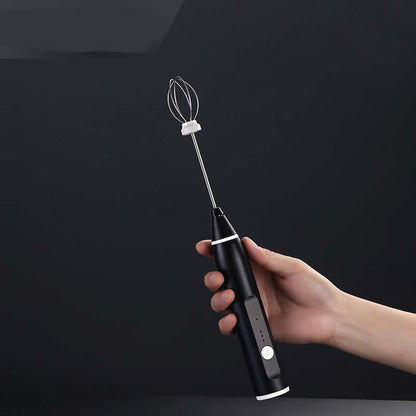 Hand holding a black electric handheld whisk with stainless steel whisk attachment