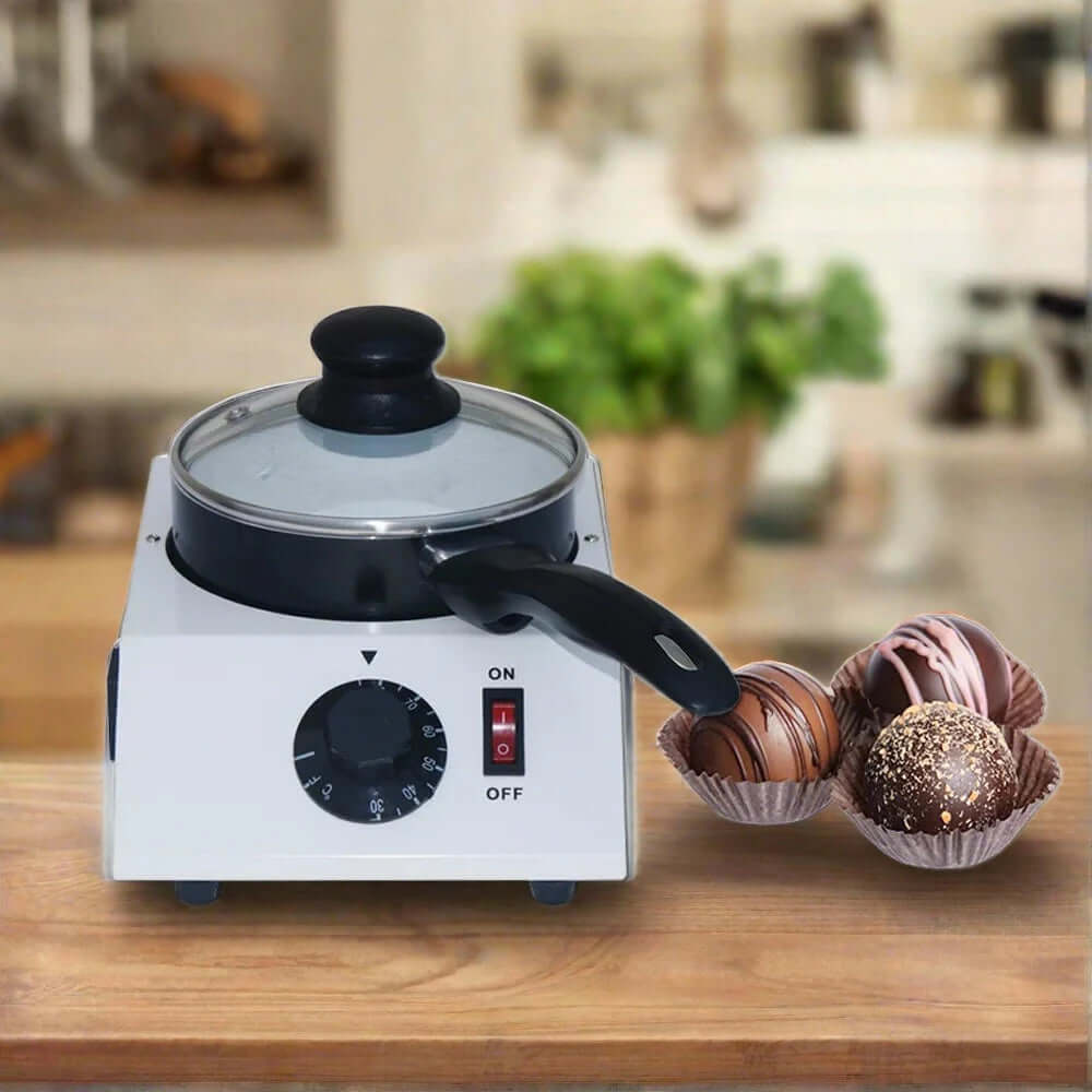 Electric chocolate melting pot with lid and assorted chocolate truffles on kitchen counter