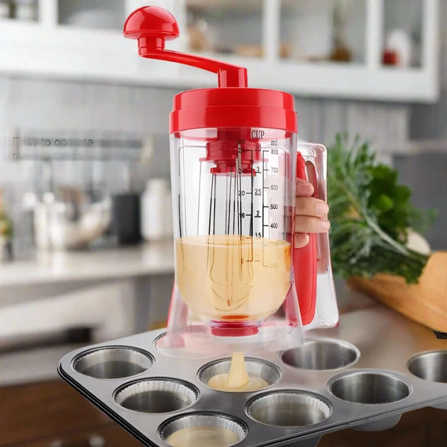 Handheld batter dispenser with red lid pouring cupcake batter into muffin tray in kitchen
