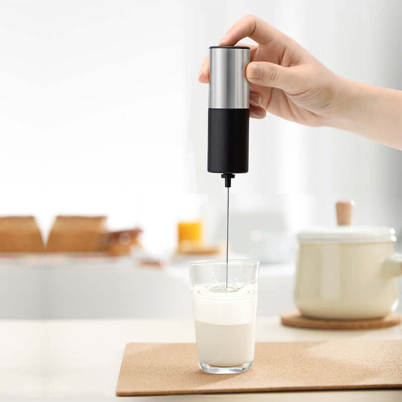 Hand using electric milk frother in glass of milk on kitchen counter