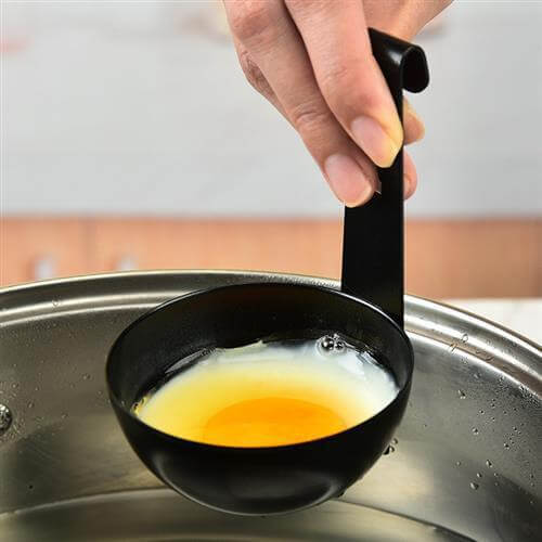 Black egg poacher spoon holding a poached egg over a pot in a kitchen setting