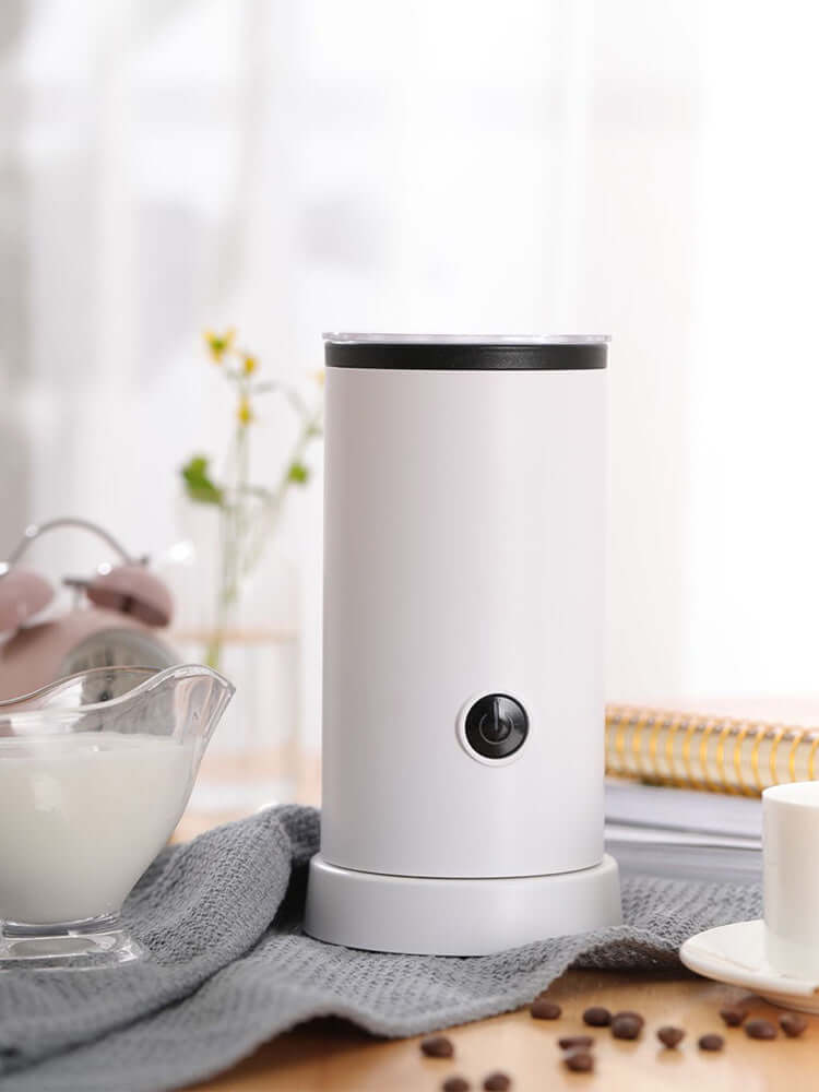Electric milk frother for coffee on kitchen counter with milk and coffee beans