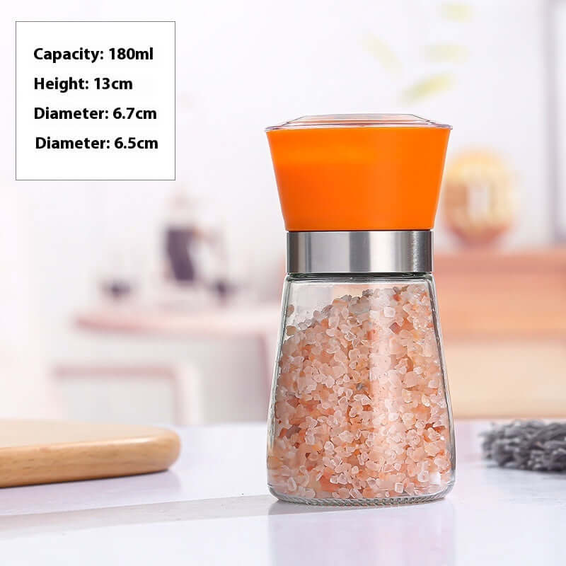 Glass spice grinder with orange lid filled with pink Himalayan salt on kitchen counter