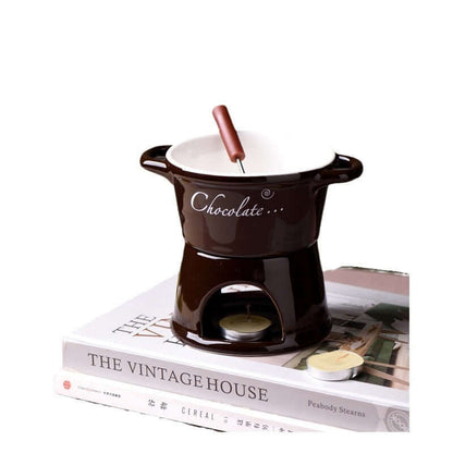 Ceramic chocolate fondue set with tealight and fork on stacked books, kitchen accessory