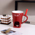 Red ceramic chocolate fondue mug set with fork, candle warmer on kitchen table