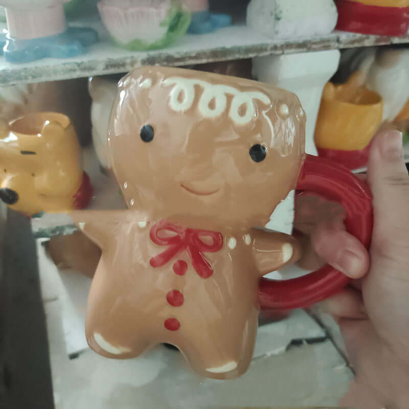 Hand holding a gingerbread man-shaped ceramic mug with red handle and festive details.