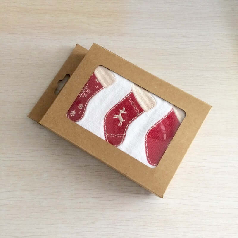 Christmas stocking patterned kitchen towels in a brown gift box on a light wood surface