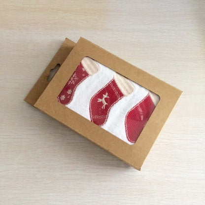 Christmas stocking patterned kitchen towels in a brown gift box on a light wood surface