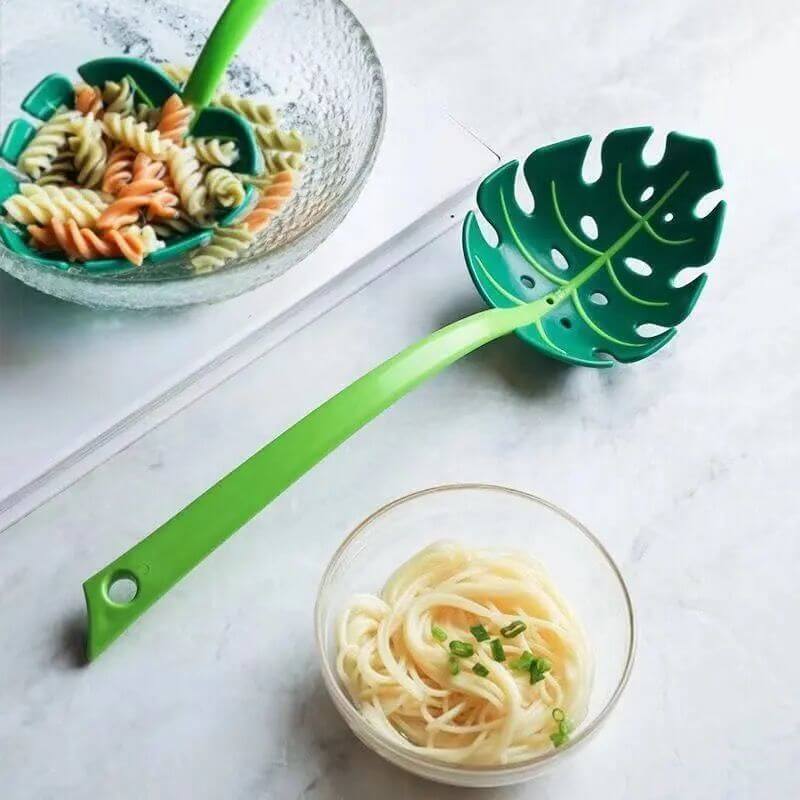 Leaf-shaped green pasta strainer spoon with cooked noodles and pasta in glass bowls