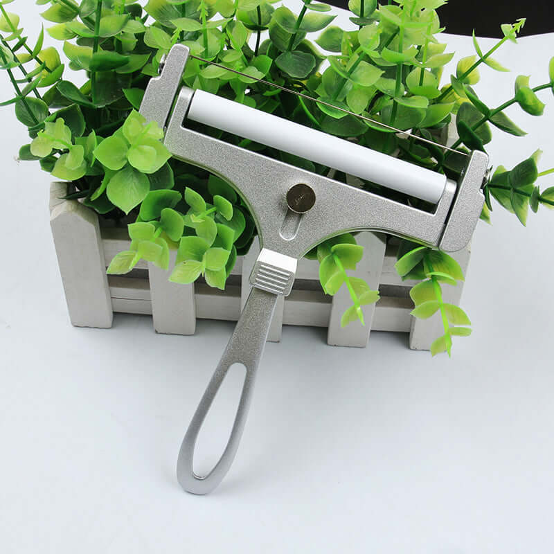 Metal tube squeezer with handle on white surface, kitchen accessory near green plant