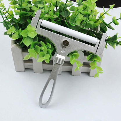 Metal tube squeezer with handle on white surface, kitchen accessory near green plant