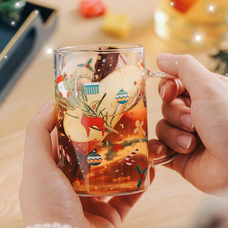 Clear glass mug with festive Christmas designs, held by hands, filled with fruit tea.