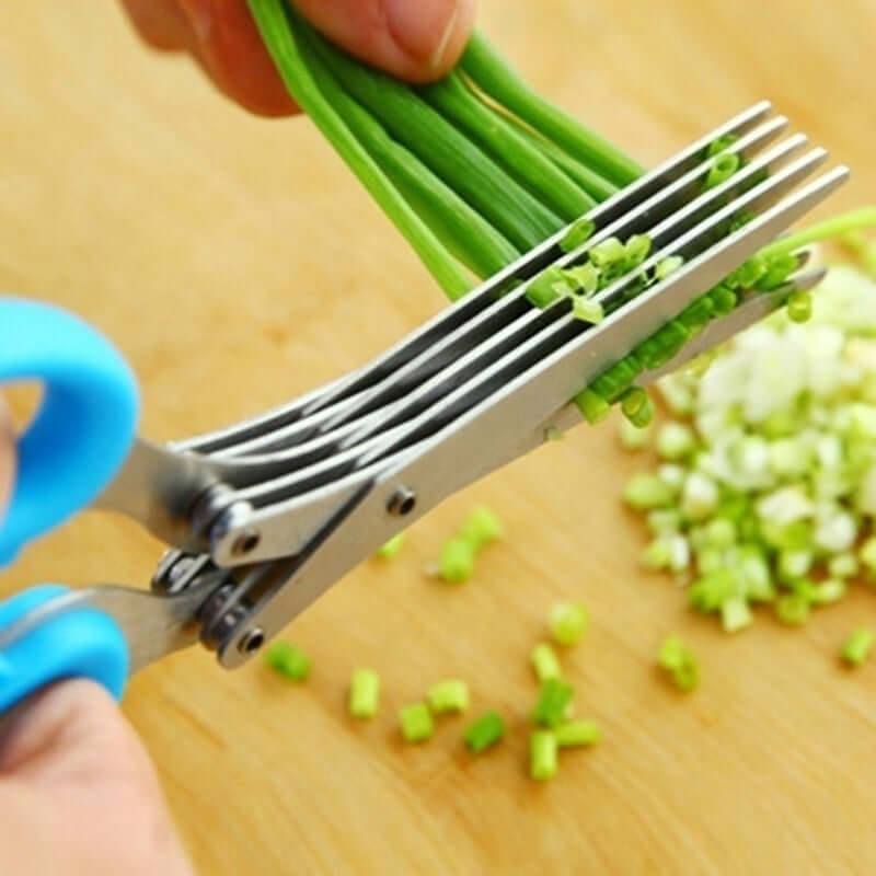 Multi-blade herb scissors with blue handle cutting fresh green onions on a wooden board