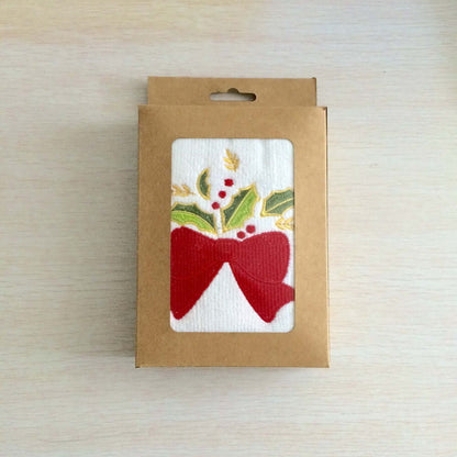 Holiday kitchen towel in gift box with red bow, holly, and berry design