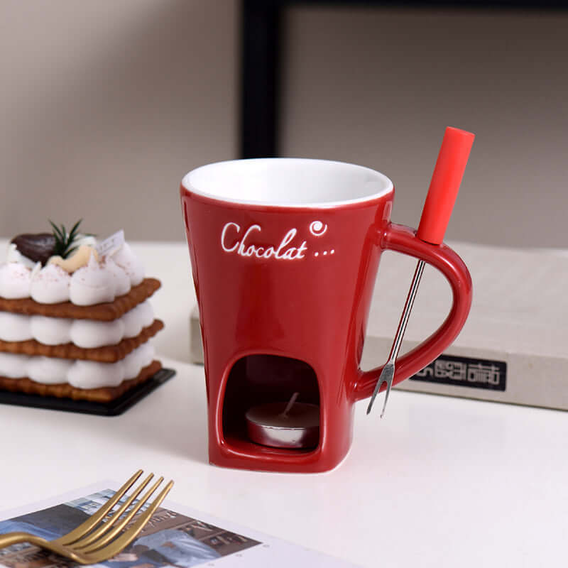 Red ceramic chocolate fondue mug with fork and tealight, kitchen accessory on table