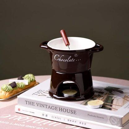 Ceramic chocolate fondue pot with fork and tealight on books, dessert in background