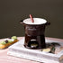 Ceramic chocolate fondue pot with fork and tealight on books, dessert in background