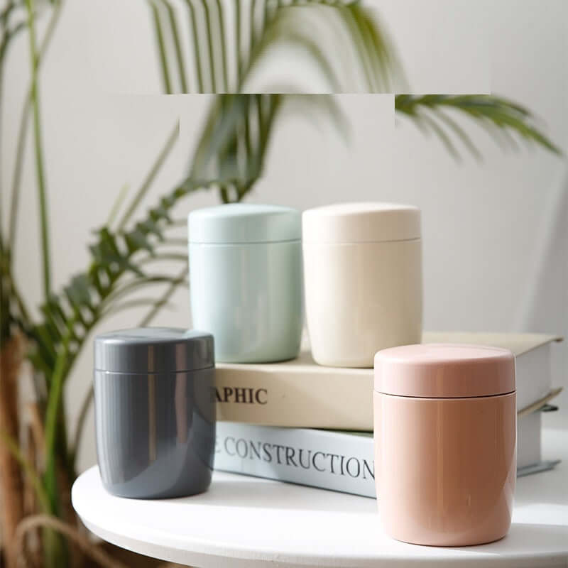 Set of four pastel kitchen storage containers on a table with books and a plant background