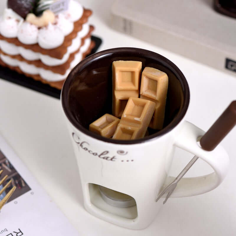 Ceramic chocolate fondue mug set with caramel chocolate pieces and fondue fork on table