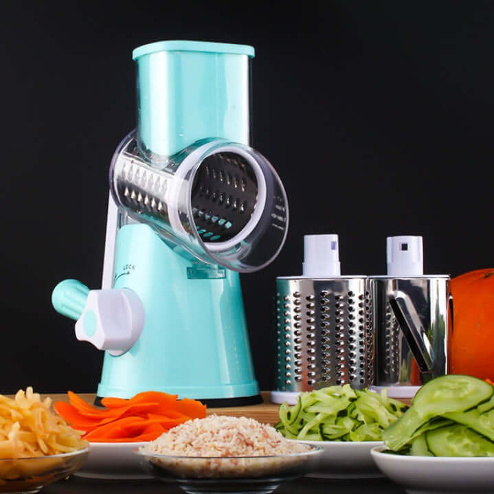 Manual rotary vegetable grater with interchangeable blades, surrounded by sliced vegetables