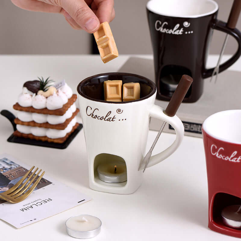 Ceramic fondue mugs with chocolate pieces, tea light candle, and dessert on a table