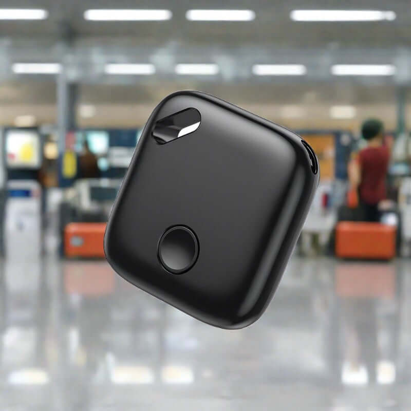 Black smart key tracker device with button, shown in airport luggage area
