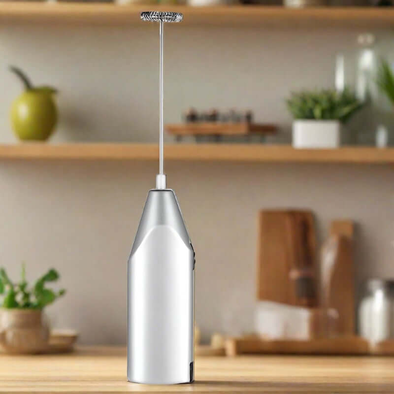 Stainless steel handheld milk frother on kitchen counter with blurred shelves in background